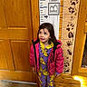 Amelia joined the competition — help win amazing prizes! child, indoor, wooden_wall, height_chart, animal_footprints, pikachu_onesie, pink_jacket, boots, curious_expression, standing, floor, door, measurement, casual_clothing, winter_wear, person, young_child, portrait, playful, colorful