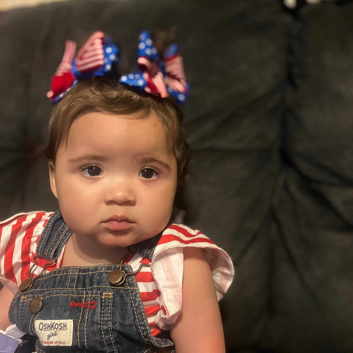 Jazaria is registered to the contest to win money with this photo: toddler, child, face, denim_overalls, bow, headband, red_white_blue, striped_shirt, sitting, indoor, couch, portrait, curly_hair, expression, cute, person, clothing, young_child, home, baby