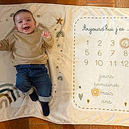 Leny participe au concours pour gagner de l'argent avec cette photo : baby, blanket, smiling, infant, clothing, jeans, sweater, rainbow, stars, floor, milestone, age_tracker, happy, cute, lying_down, child, indoors, playful, soft_texture, portrait