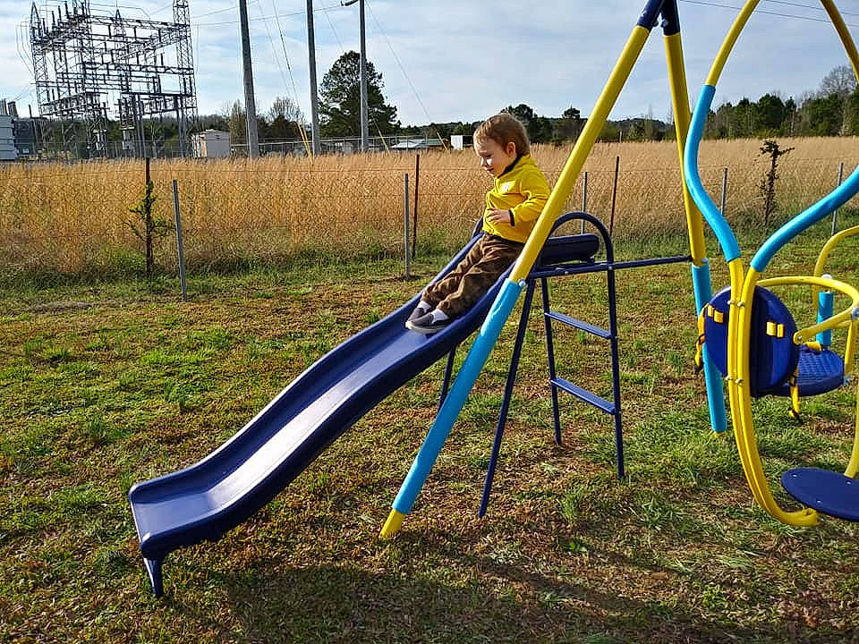 Zachary is registered to the contest to win money with this photo: chute, city, fun, grass, human_settlement, leisure, outdoor_play_equipment, person, plant, play, playground, playground_slide, public_space, recreation, sky, swing, tree