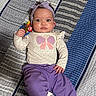 baby, child, infant, portrait, lying_down, bed, quilt, striped_blanket, headband, bow, butterfly_shirt, purple_pants, white_socks, teething_toy, toy, wide_eyes, face, indoors, smiling, colorful_clothing