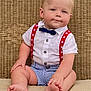 baby, child, sitting, barefoot, bow_tie, suspenders, striped_shorts, white_shirt, wicker_background, cushion, cute, portrait, blue_eyes, blond_hair, indoor, plump, smiling, person, fashion, toddler