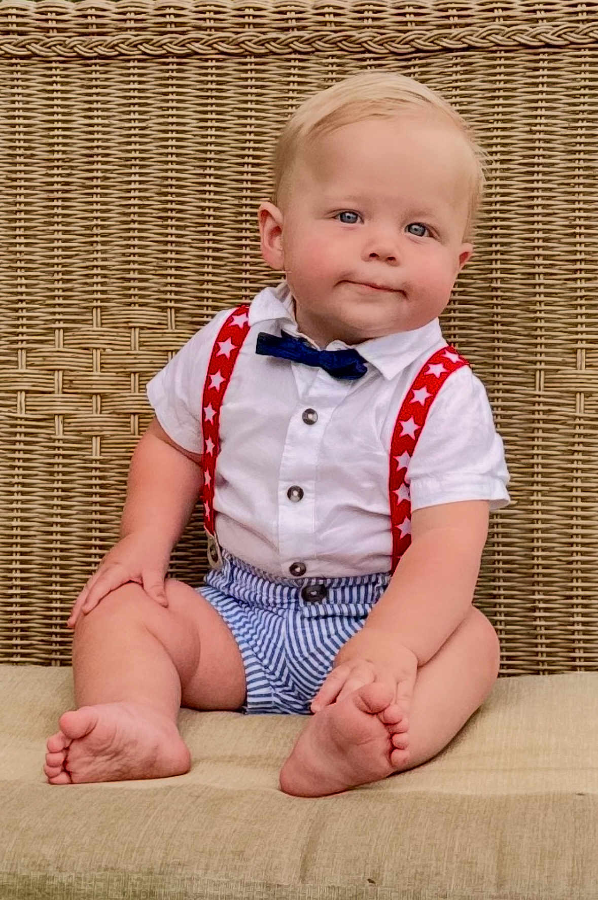 Finley is registered to the contest to win money with this photo: baby, child, sitting, barefoot, bow_tie, suspenders, striped_shorts, white_shirt, wicker_background, cushion, cute, portrait, blue_eyes, blond_hair, indoor, plump, smiling, person, fashion, toddler