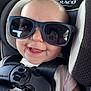 Ainsley is registered to the contest to win money with this photo: baby, car_seat, sunglasses, smile, happy, child, seatbelt, reflection, face, infant, closeup, safety_harness, cute, person, casual_clothing, headrest, indoor, portrait, baby_clothes, black_straps