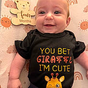 Ainsley is registered to the contest to win money with this photo: baby, infant, smiling, black_shirt, giraffe, cute, lying_down, four_months, patterned_blanket, sun, rainbow, cloud, wooden_sign, happy, child, face, eyes, cute_clothing, baby_gesture, indoor