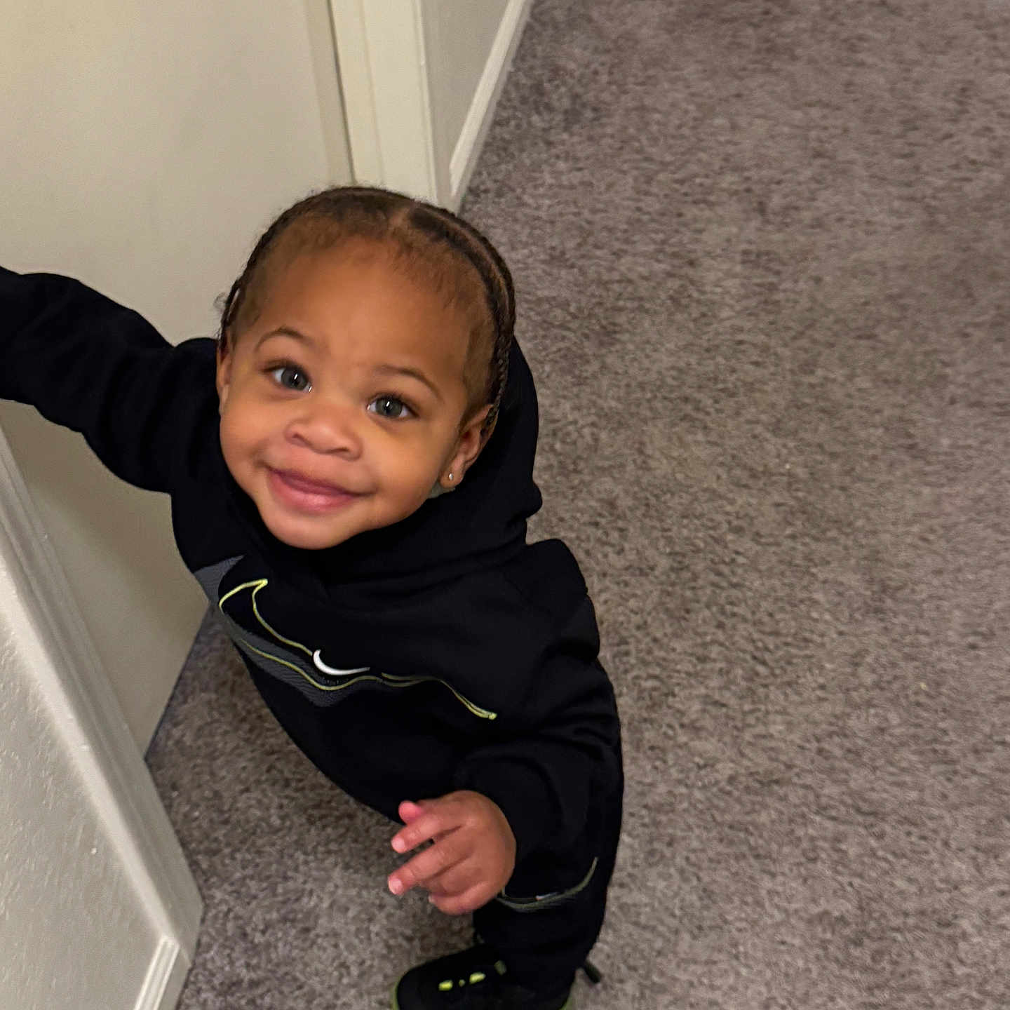 Syncere joined the competition — help win amazing prizes! black_hoodie, braided_hair, carpet, child, curious, cute, earrings, happy, indoor, joyful, light_skin_tone, person, playful, portrait, small_hand, smiling, sneakers, standing, toddler, young_child