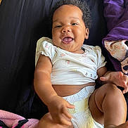 Nayeli Dawson is registered to the contest to win money with this photo: baby, infant, child, smiling, happy, portrait, lying_down, bed, blanket, purple, black, floral_clothing, diaper, short_sleeves, curly_hair, outdoorless, closeup, human, family, photography