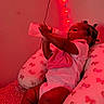 baby, infant, child, bottle, feeding, milk, sitting, pillow, butterfly_pattern, bedroom, fairy_lights, red_lighting, indoor, portrait, braids, onesie, blanket, cushion, relaxed, photography