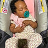 baby, sleeping, pacifier, car_seat, infant, portrait, indoors, pink, heart_pattern, clothing, blanket, curly_hair, closed_eyes, peaceful, hands, safety_labels, automotive, seated, adorable, photography