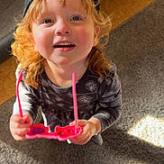 Elizabeth Rae joined the competition — help win amazing prizes! toddler, child, curly_hair, cap, pink_sunglasses, carpet, indoor, smiling, happy, looking_up, person, clothing, shadow, sunlight, floor, footwear, red_pants, green_sandals, playful, casual