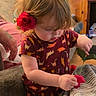 toddler, child, flower, red_flower, rose, curly_hair, indoor, couch, blanket, striped_blanket, wooden_wall, hand, dinosaur_print_dress, person, young_child, cozy, home_interior, soft_lighting, cute, exploring