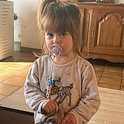Eléana Hita Cortes participe au concours pour gagner de l'argent avec cette photo : toddler, child, pacifier, plush_toy, indoor, girl, long_hair, brown_hair, sweatshirt, deer_graphic, toy, furniture, wooden_cabinet, tile_floor, curious_expression, standing, cozy, casual_clothing, home, natural_light