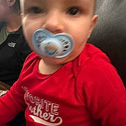 Destinee is registered to the contest to win money with this photo: adult, baby, casual_clothing, child, close_up, couch, eyes, face, family, front_facing, head, home, indoors, infant, pacifier, photograph, portrait, red_shirt, sitting, toddler