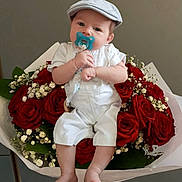 Gabriel participe au concours pour gagner de l'argent avec cette photo : baby, infant, pacifier, cap, white_overalls, roses, bouquet, flowers, red_roses, green_leaves, hand, bracelet, cute, portrait, indoor, flower_arrangement, child, sitting, soft_lighting, neutral_background