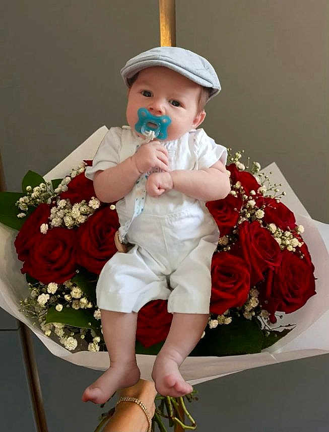 Gabriel participe au concours pour gagner de l'argent avec cette photo : baby, infant, pacifier, cap, white_overalls, roses, bouquet, flowers, red_roses, green_leaves, hand, bracelet, cute, portrait, indoor, flower_arrangement, child, sitting, soft_lighting, neutral_background