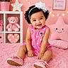 baby, child, pink, dress, shoes, headband, smile, curly_hair, teddy_bear, plush_toy, star_lights, heart_lights, star_pillow, rug, flowers, room_decor, frame, sitting, happy, indoors