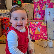 Lya a rejoint le concours — aidez-le/la à gagner de superbes lots ! baby, child, christmas_tree, presents, gift_wrap, red_dress, white_tights, smiling, sitting, floor, holiday, indoors, festive, bow, cute, toys, shoes, happy, portrait, celebration