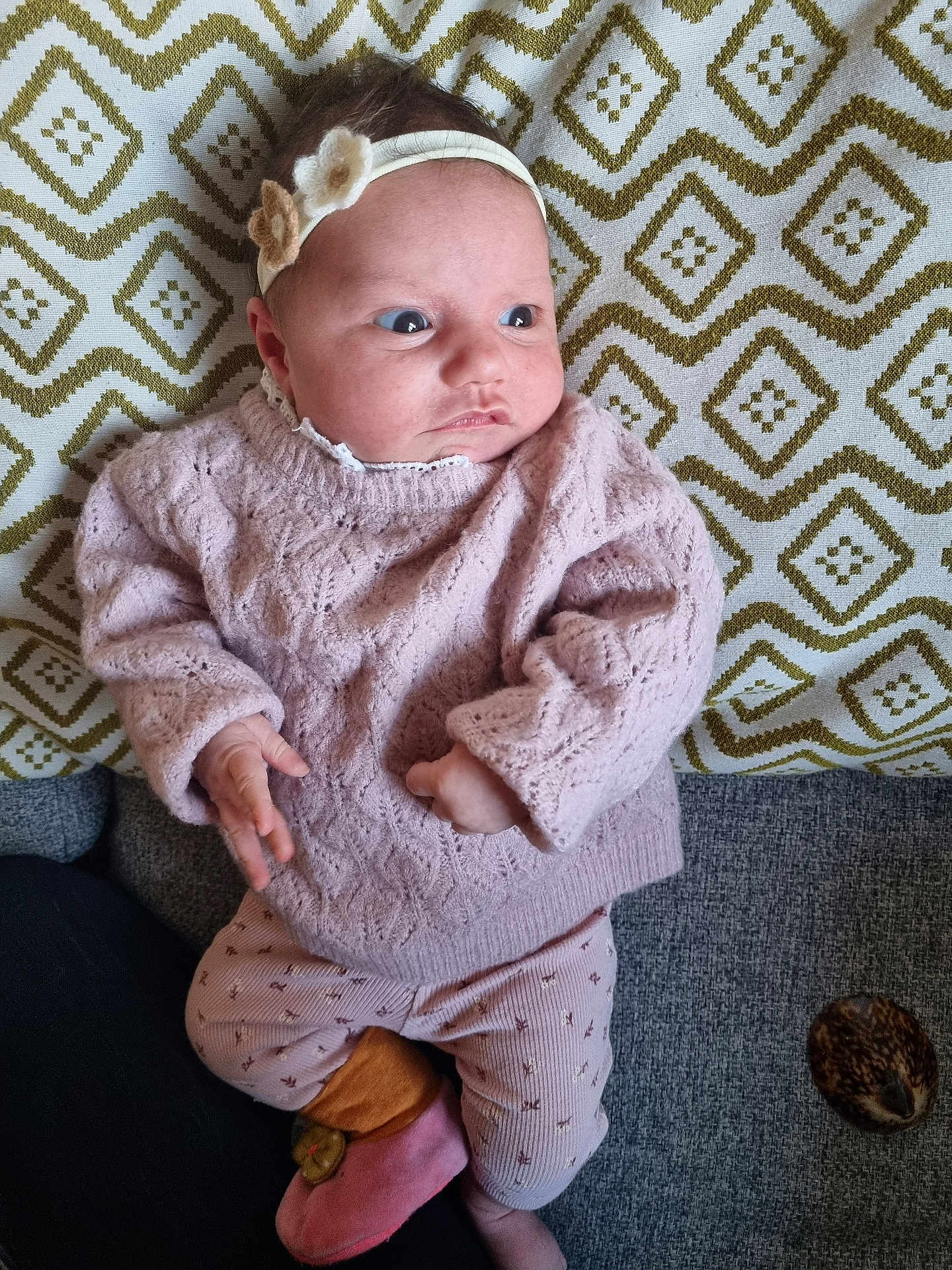 Joséphine participe au concours pour gagner de l'argent avec cette photo : baby, infant, headband, flower, pink_sweater, patterned_pants, slippers, blanket, geometric_pattern, couch, texture, indoor, cute, child, young, portrait, cozy, warm_colors, lying_down, curious