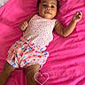 baby, child, infant, portrait, smiling, lying_down, bed, blanket, pink, colorful, clothing, polka_dots, floral_pattern, heart, home, indoor, curly_hair, dark_skin, happy, photography
