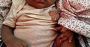 Sy'Meer Lopez is registered to the contest to win money with this photo: adult_hand, baby, blanket, child, close_up, clothing, eyes, face, feet, hair, hand, indoor, infant, legs, lying_down, newborn, onesie, patterned_fabric, portrait, skin