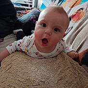 Johann a rejoint le concours — aidez-le/la à gagner de superbes lots ! baby, child, infant, couch, blanket, pillow, face, expression, wide_eyes, mouth_open, clothing, indoor, furniture, person, hand, head, soft_texture, colorful, home, background
