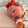 baby, newborn, infant, child, portrait, lying_down, headband, orange_clothing, onesie, smiling, face, eyes, hands, cushion, soft_surface, indoors, close_up, nursery, resting, adorable