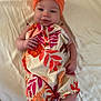 baby, infant, child, bed, blanket, headband, orange, romper, floral_pattern, smile, cute, portrait, skin, hands, feet, clothing, indoors, light, person, lying_down
