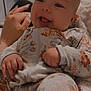 baby, infant, smiling, face, hand, onesie, floral_pattern, clothing, blanket, cozy, cute, happy, tongue_out, person, soft_lighting, indoor, skin, nail_polish, comfort, relaxation