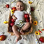 baby, basket, apple, flower, yellow_flower, white_flower, blanket, smiling, happy, infant, clothing, shorts, white_shirt, skin, foot, hand, head, cheerful, lying_down, indoors