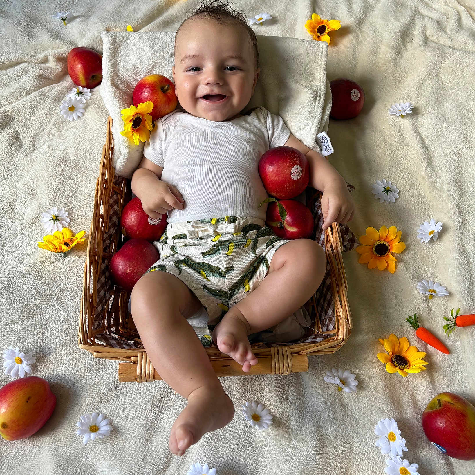 Elio participe au concours pour gagner de l'argent avec cette photo : apple, baby, basket, blanket, cheerful, clothing, flower, foot, hand, happy, head, indoors, infant, lying_down, shorts, skin, smiling, white_flower, white_shirt, yellow_flower