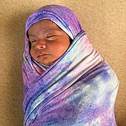 Cochise is registered to the contest to win money with this photo: baby, blanket, blue, child, close_up, cozy, face, head, indoors, infant, newborn, peaceful, portrait, purple, resting, sleeping, soft, swaddled, tie_dye, wrapped