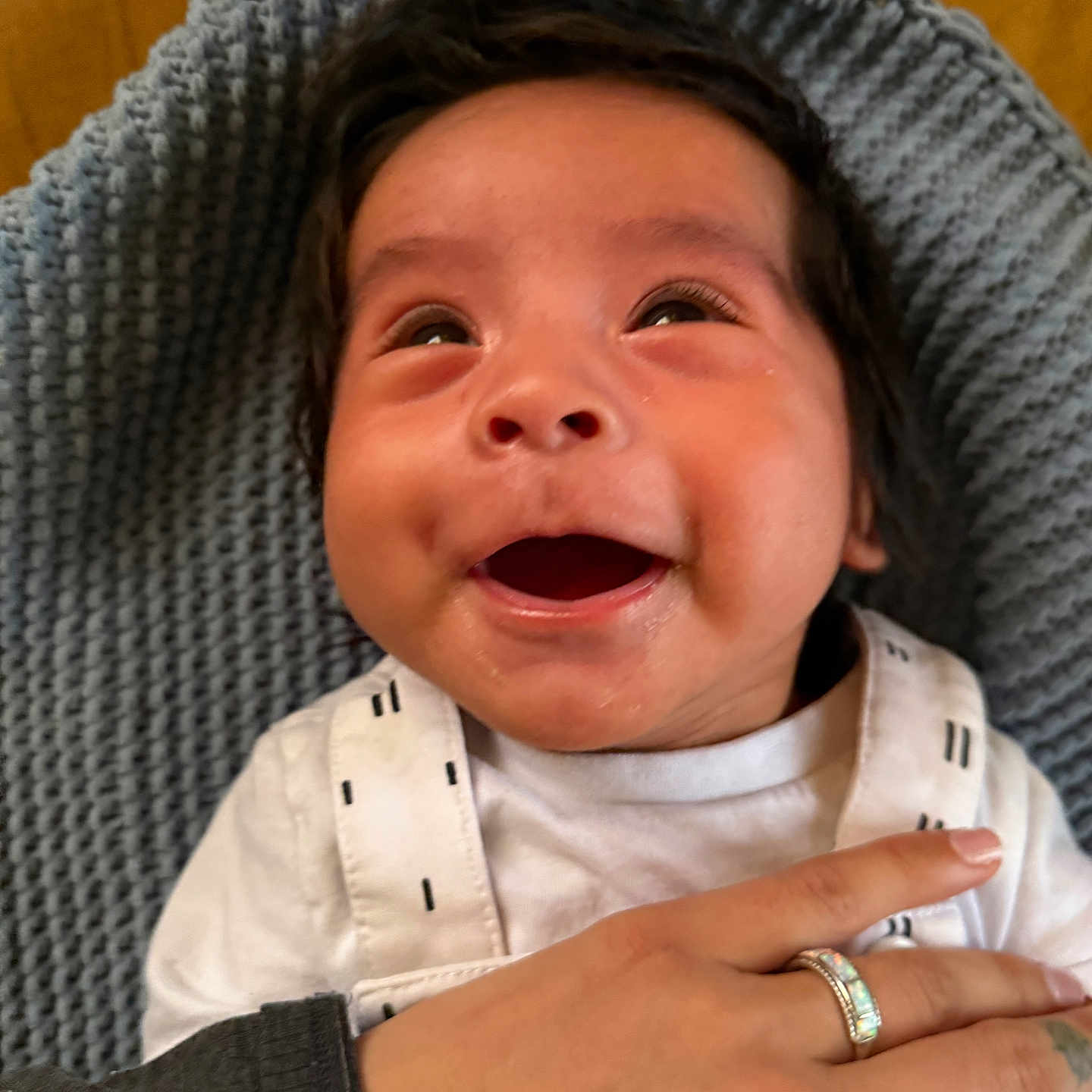 Cochise is registered to the contest to win money with this photo: baby, child, closeup, cozy, cute, expressive, face, hand, happy, indoor, infant, knitted_blanket, looking_up, person, portrait, smiling, tender, warm, white_clothing, young