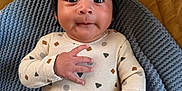 Cochise is registered to the contest to win money with this photo: baby, child, clothing, cozy, curious, cute, face, hand, head, indoors, infant, knitted_blanket, lying_down, patterned_shirt, person, portrait, purple_pants, smiling, soft_texture, young