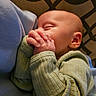 baby, sleeping, hands, clasped_hands, green_clothing, blue_fabric, face, peaceful, infant, portrait, closeup, soft_light, cozy, patterned_background, cute, newborn, skin, ear, resting, child
