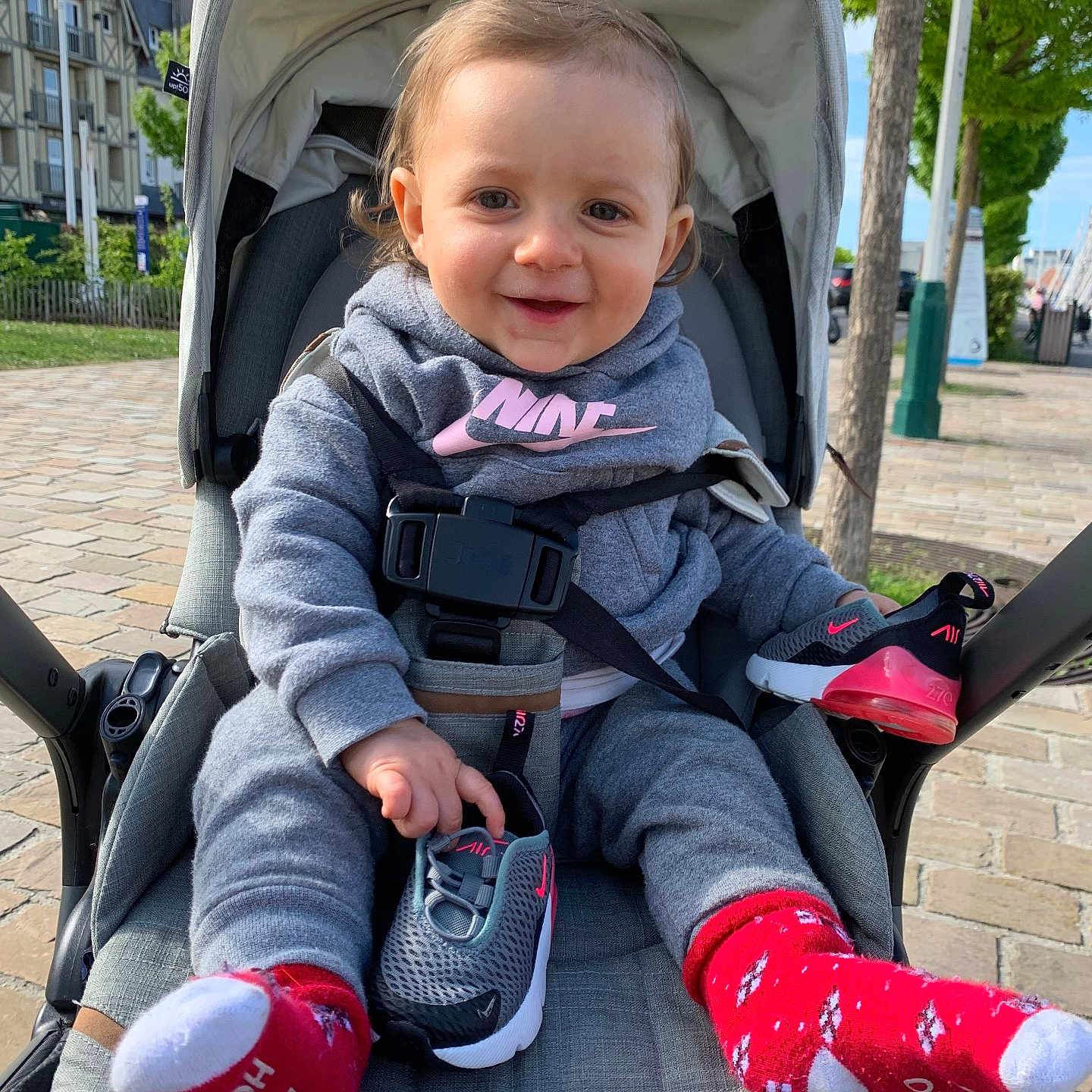 Celeyne a rejoint le concours — aidez-le/la à gagner de superbes lots ! baby, building, casual_clothing, child, daylight, footwear, happy, hoodie, outdoor, person, playful, seatbelt, shoe, sidewalk, smile, socks, stroller, toddler, tree, urban