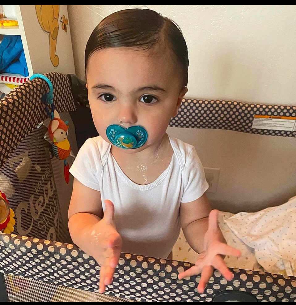 Maxmillian is registered to the contest to win money with this photo: child, baby, toddler, pacifier, playpen, onesie, hands, big_eyes, slicked_hair, toy, crib, polka_dot, blanket, indoor, portrait, drool, curious_expression, gripping_rail, face, nursery