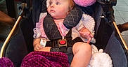 Liliana is registered to the contest to win money with this photo: baby, child, infant, stroller, portrait, sitting, wide_eyed, red_hair, pink_clothing, purple_blanket, plush_blanket, travel_pillow, pacifier, harness, carriage, indoor, kitchen, table, tile_floor, cozy