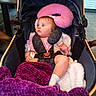 baby, child, infant, stroller, portrait, sitting, wide_eyed, red_hair, pink_clothing, purple_blanket, plush_blanket, travel_pillow, pacifier, harness, carriage, indoor, kitchen, table, tile_floor, cozy