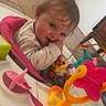 baby, child, infant, smiling, sitting, activity_center, baby_toys, colorful_toys, highchair, playtime, indoor, portrait, face, hands, brown_hair, long_sleeves, pink, orange, plastic, home