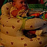 baby, infant, child, sitting, activity_seat, inflatable_chair, toy, colorful_toys, portrait, face, looking_sideways, indoors, living_room, warm_lighting, low_light, phone_screenshot, lock_screen, clock, blanket, safe
