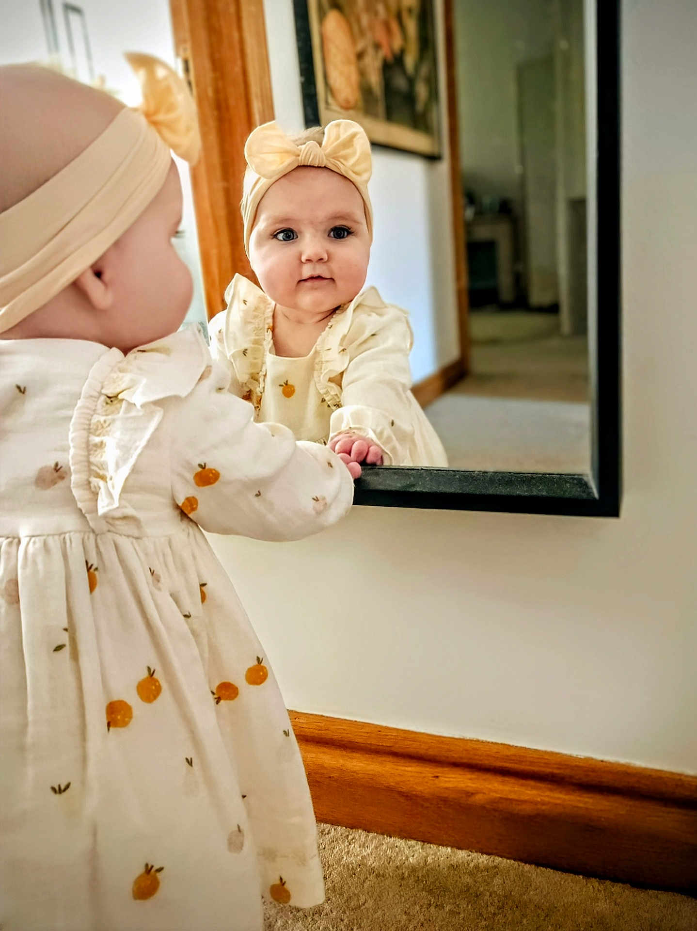 Florence joined the competition — help win amazing prizes! baby, child, girl, mirror, reflection, headband, dress, curious, indoor, carpet, wooden_trim, wall, hand, face, portrait, clothing, home, soft_light, cute, infant