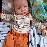 Blake is registered to the contest to win money with this photo: baby, infant, child, clothing, striped_shirt, orange_pants, blanket, patterned_blanket, animal_print, lying_down, looking_at_camera, indoor, cute, young_child, sleeping_area, soft_toys, fabric, face, head, person
