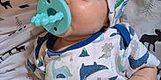 Blake is registered to the contest to win money with this photo: baby, infant, pacifier, hat, onesie, dinosaur_print, blanket, animal_pattern, moose, tree_pattern, cute, child, portrait, laying_down, clothing, hand, face, indoor, newborn, soft_lighting