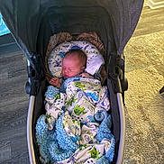 Walker is registered to the contest to win money with this photo: baby, blanket, stroller, sleeping, indoor, infant, cozy, soft, colorful, dinosaur, child, person, carriage, comfort, head, face, clothing, floor, home, rest