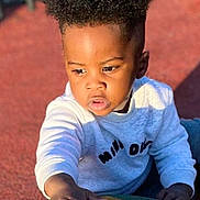 Grâce Miguel participe au concours pour gagner de l'argent avec cette photo : child, toddler, curly_hair, sweater, outdoor, playground, sunlight, hand, face, expression, texture, colorful, young, person, casual_clothing, daylight, skin, portrait, activity, curiosity