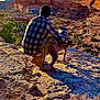 person, dog, canyon, cliff, rock, landscape, outdoors, hiking, sunset, sky, mesa, beanie, plaid_shirt, companionship, pet, shadow, nature, trail, scenic, adventure