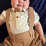 baby, infant, smile, face, clothing, bow_tie, suspenders, beige, shorts, pillow, blue, cute, chubby, skin, person, young_child, indoors, portrait, seated, happy