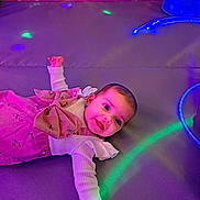 Neveah is registered to the contest to win money with this photo: baby, child, smiling, purple, dress, bow, floral, lights, disco, indoor, happy, cute, infant, person, portrait, colorful, fabric, lying_down, face, playful