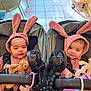 baby, bunny_ears, pink_clothing, stroller, twin_babies, stuffed_animal, fan, indoor, tile_floor, cute, child, infant, face, headwear, seated, toy, adorable, matching_outfits, black_fan, happy