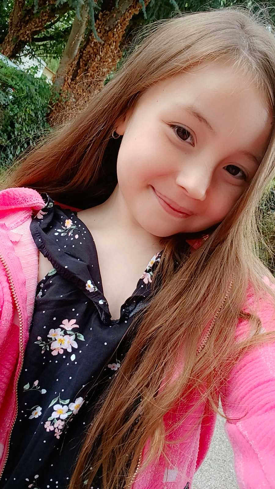 Lucinda participe au concours pour gagner de l'argent avec cette photo : child, girl, smiling, portrait, long_hair, outdoor, nature, tree, greenery, pink_jacket, floral_dress, face, happy, earring, casual_clothing, daylight, person, cute, young, fashion